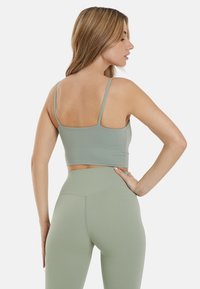 Grøn sports crop top med tynde stropper, glat tekstur og tætsiddende design, parret med højtaljede matchende leggings.