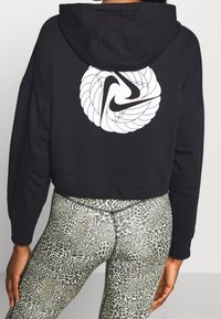 Hoodie noir cropped avec un logo en spirale blanc au dos. Associé à un legging en imprimé léopard vert. Tissu doux, coupe ample.