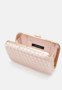 Tkany jasnoróżowy kopertówka z metaliczną złotą ramką, z zapięciem na zatrzask i miękką podszewką z tkaniny, wewnątrz oznaczona napisem "ANNA FIELD".