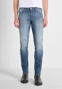 Vaqueros ajustados de un azul claro con un acabado desgastado, diseño de cinco bolsillos y herrajes de metal. Combinados con botas negras hasta el tobillo.