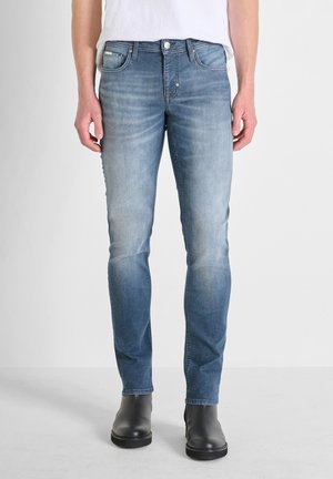 Light blue slim-fit jeans with a faded finish, five-pocket design, and metal hardware. Paired with black ankle boots.
