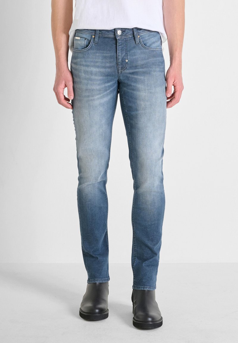 Vaqueros ajustados de un azul claro con un acabado desgastado, diseño de cinco bolsillos y herrajes de metal. Combinados con botas negras hasta el tobillo.