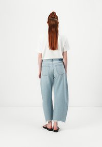 Lichtblauwe wijde jeans met rafelige zomen, van katoen, hoge taille, achterzakken, gecombineerd met een wit T-shirt met korte mouwen en sandalen.