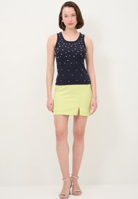 Námořnický top bez rukávů s perlovými ozdobami, spárovaný se světle zelenou mini sukní s předním rozparkem. Vzhled doplňují stříbrné sandály na podpatku.
