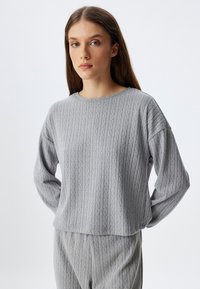 Heather grijze gebreide sweatshirt met geribbelde textuur, ronde hals en lange mouwen, gecombineerd met een bijpassende onderkant in een vergelijkbaar ontwerp.