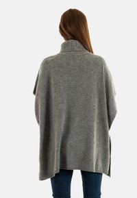 Poncho de lana gris de punto con cuello alto y silueta relajada. Cuenta con aberturas laterales y puños acanalados, ofreciendo una textura suave.