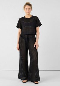 Conjunto de dos piezas de punto abierto en negro que presenta una blusa corta con mangas cortas y pantalones de pierna ancha, enfatizando un diseño suelto y transpirable.