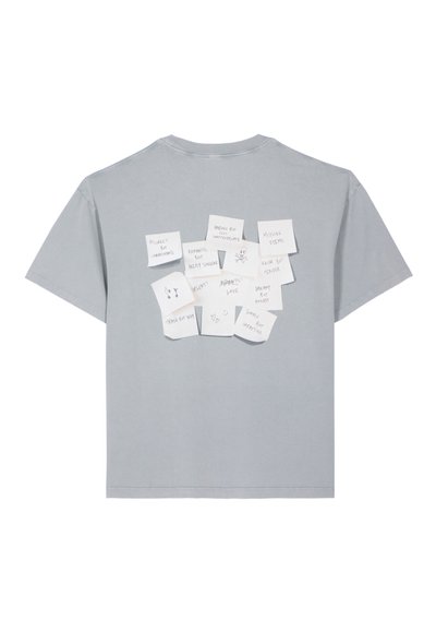 Camiseta de algodón gris con un corte relajado, que presenta varias notas adhesivas blancas con frases escritas a mano en la parte de atrás. Mangas cortas, cuello redondo.