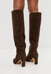 Stivali al ginocchio in suede marrone con un design strutturato, punta rotonda e tacco modesto. Presentano una cerniera laterale per una facile vestibilità.