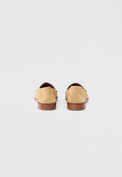 Μοκασίνια από καφέ σουέτ με στρογγυλεμένη μύτη, χαμηλό ξύλινο τακούνι και διακοσμητικές χάντρες στο πίσω μέρος. Απλός και λιτός σχεδιασμός.