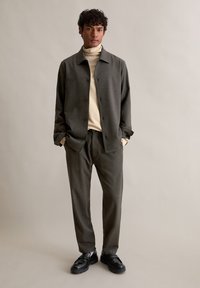 Szary żakiet przypominający wełnę założony na kremowy golf, w połączeniu ze współczesnymi szarymi spodniami oraz czarnymi loafersami, z dodatkowymi detalami przy guzikach i kieszeniach.