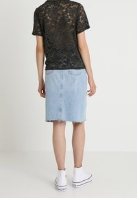 Camiseta de encaje negra con patrón floral, combinada con una falda de mezclilla azul clara con dobladillo deshilachado y bolsillos traseros, usada con zapatillas blancas.