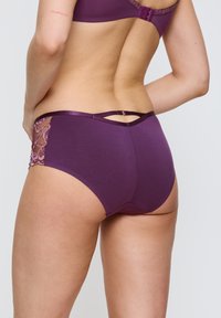 Fialové bavlněné spodní prádlo s krajkovými detaily po stranách, které má tenký saténový pásek v pase a dvojitý pásový akcent na zadní části.