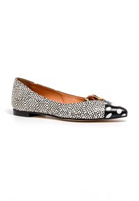 Zapato plano de lunares en blanco y negro con puntera de charol negro en forma de punta. Presenta una textura suave y un diseño de perfil bajo.