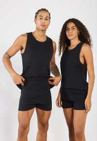 Dos modelos llevan tops de tirantes negros con textura y pantalones cortos, presentando un diseño ajustado, escote redondo y detalles de botones en los pantalones.