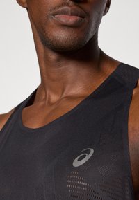 Μαύρο αθλητικό αμάνικο μπλουζάκι φτιαγμένο από αναπνέον ύφασμα, με υφή και ανακλαστικό λογότυπο στην αριστερή περιοχή του στήθους.