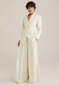 Lichtgekleurde, linnenmix pak met een op maat gemaakte blazer met één knoop en wijde broekspijpen met plooien, wat een formele uitstraling biedt.