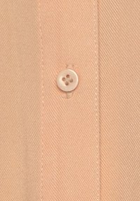 Peach-colored fabric close-up featuring diagonal texture, a round white button with four holes, and a seam on the left side.