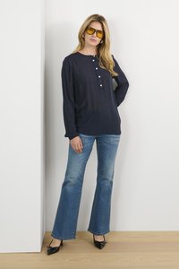 Blouse bleu marine à manches longues avec patte de boutonnage, associée à un jean flare bleu clair et des escarpins noirs à bout pointu. Des lunettes de soleil teintées jaunes mettent en valeur le look.