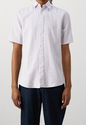 Mand iført en kortærmet lyserød og hvid vertikalt stribet skjorte med mørkeblå bukser mod en ensfarvet baggrund.