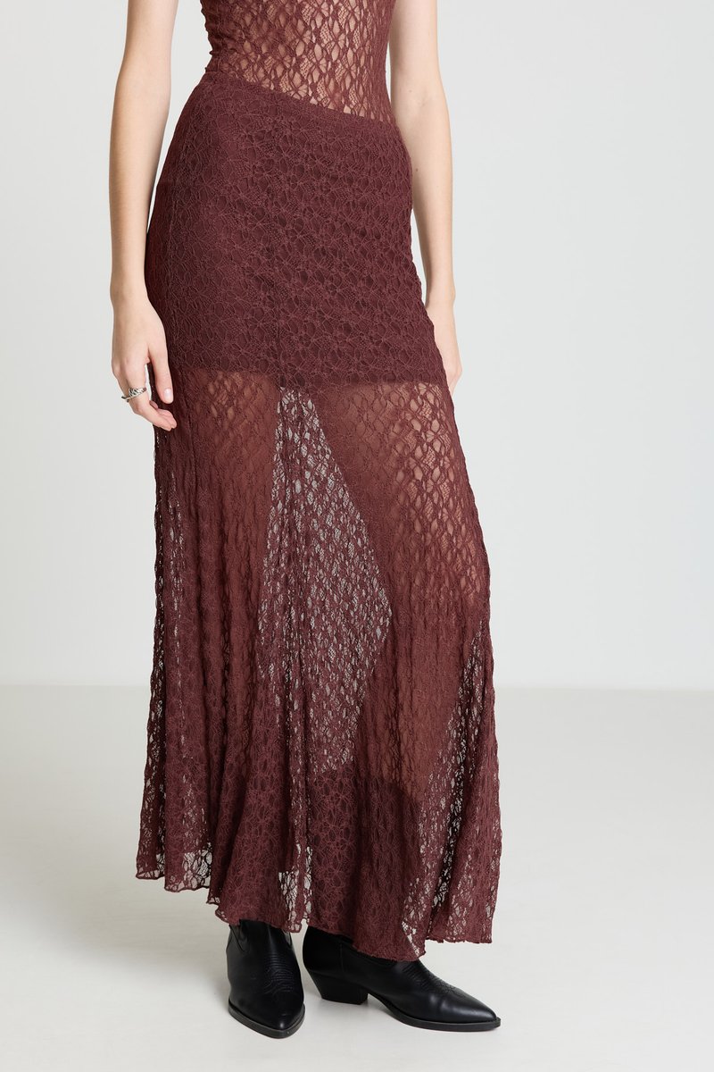 Burgundy lace maxi skirt with a sheer overlay, featuring a diamond pattern and a high slit. Paired with black ankle boots.