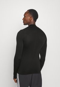 Langärmliges schwarzes Oberteil aus dehnbarem Stoff, mit hohem Kragen und figurbetonter Silhouette, sowie dezenten Nahtdetails auf der Rückseite.
