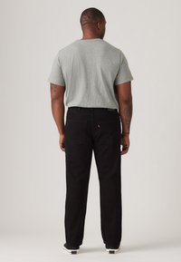 Zwarte denim broek met een rechte pasvorm, gecombineerd met een grijs shirt met korte mouwen. Voorzien van stiksels en achterzakken. Gestyled met casual sneakers.