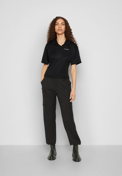 Polo shirt preto de manga curta com colarinho, combinado com calças cargo pretas com bolsos laterais e botas de borracha verdes até ao tornozelo.