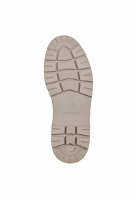 Suela de zapato de goma beige con bandas prominentes, surcos y un logotipo circular; textura suave, diseño robusto y área del talón reforzada.