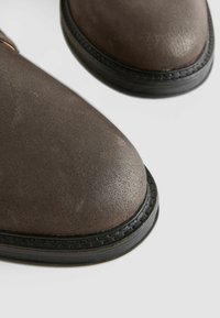Brown leather boots with a textured finish, rounded toes, and black rubber soles. Includes a decorative stitched welt around the base.