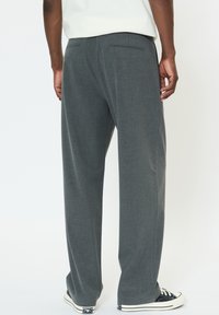 Sivé nohavice s širokými nohavicami vyrobené z mäkkej látky, s hladkou textúrou a jemným vzorom, s dvoma zadnými vreckami a kontrastnými teniskami.