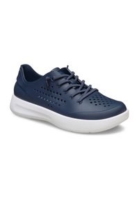 Zapatilla deportiva de color azul marino, hecha de material sintético con diseño perforado, suela blanca y cordones oscuros. Presenta una textura suave y una forma redondeada.
