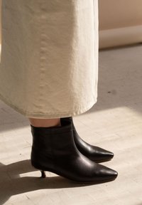 Juodi odiniai aulinukai su smailia nosimi ir mažu, plonu kulnu, derinami su šviesios spalvos audinio sijonu.