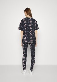 Conjunto de pijama combinando com um fundo preto decorado com padrões de renas e flocos de neve. Feito de um tecido suave, inclui uma t-shirt larga e leggings ajustadas.