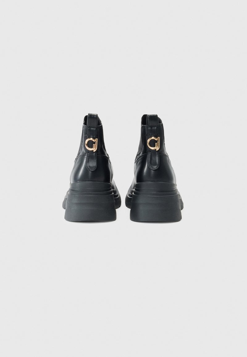 Bottines noires en cuir avec une semelle épaisse, dotées d'un accent logo doré et d'un détail texturé à l'arrière.