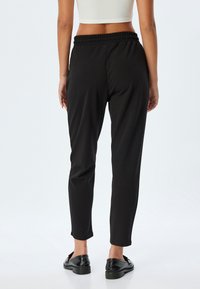 Schwarze, elastische Hose mit schmalem Design und glatter Textur. Bietet eine bequeme Passform und keine Taschen, kombiniert mit schwarzen Schuhen.