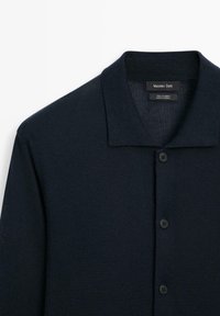 Mörk marinblå kashmirkofta med en enkel krage, fem svarta knappar och en mjuk textur. Märkesskylten säger "Massimo Dutti."