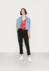 Casaco de ganga com embellishments florais sobre uma blusa floral vermelha, combinado com calças pretas ajustadas e ténis brancos de plataforma.
