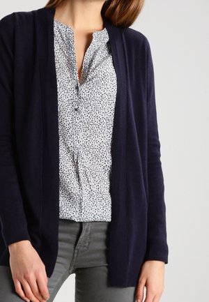 Navy blue cardigan made of soft knit fabric, open front design, paired with a white shirt featuring a black dot pattern, gray pants.