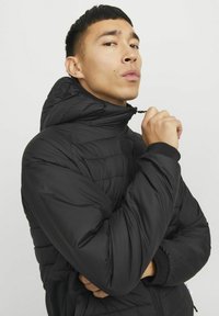 Chaqueta negra acolchada con cremallera y cuello alto, con puños ajustados. Presenta una textura suave y un diseño liviano, adecuado para superponer.