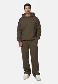 Oliwkowy hoodie i dopasowane spodnie wykonane z miękkiego materiału. Posiada przednią kieszeń, ściągacze na rękawach oraz logo tekstowe na piersi i nodze.