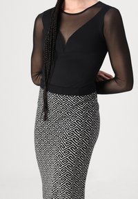 Body noir avec des manches longues transparentes et un décolleté en V, assorti à une jupe crayon noire et blanche à motifs présentant un design géométrique.