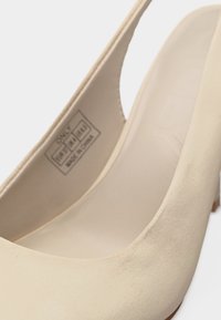 Μπεζ γόβα από σουέντ με στρογγυλερή μύτη, χαμηλό τακούνι και ετικέτα που αναγράφει «Only, 100% PU, Κατασκευάστηκε στην Κίνα» στο εσωτερικό του παπουτσιού.