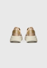 Vue arrière de baskets beiges avec une tige texturée, un accent doré sur le talon et une semelle épaisse de couleur crème.