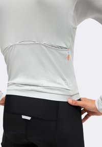 Gros plan d'une personne portant un haut à manches longues gris clair avec des poches à l'arrière et un short de cyclisme noir avec rembourrage et détails de couture.