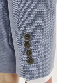 Jasnoniebieska teksturowana tkanina żakietu z czterema ciemnymi guzikami przy mankietach. Design charakteryzuje się drobnym splotem i widocznym ściegiem.