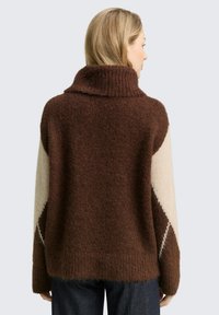 Bruine en crèmekleurige kleurbloktrui met een hoge kraag, textuur gebreid en een oversized pasvorm. Heeft een schuin diamantpatroon op de mouwen.