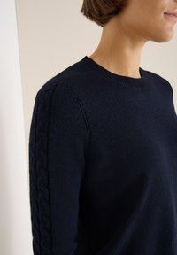 Marineblauer Strickpullover mit klassischem Rundhalsausschnitt und strukturiertem Zopfmuster entlang der Ärmel. Weicher, glatter Stoff.