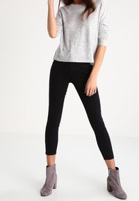 Szary melanżowy, długi rękaw top zestawiony z czarnymi dopasowanymi spodniami i szarymi botkami za kostkę. Strój charakteryzuje się luźnym krojem i prostym designem.