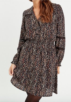 Robe noire à motif floral crème, rouge et marron. Présente un col en V, des manches longues et une taille cintrée pour une silhouette ajustée.